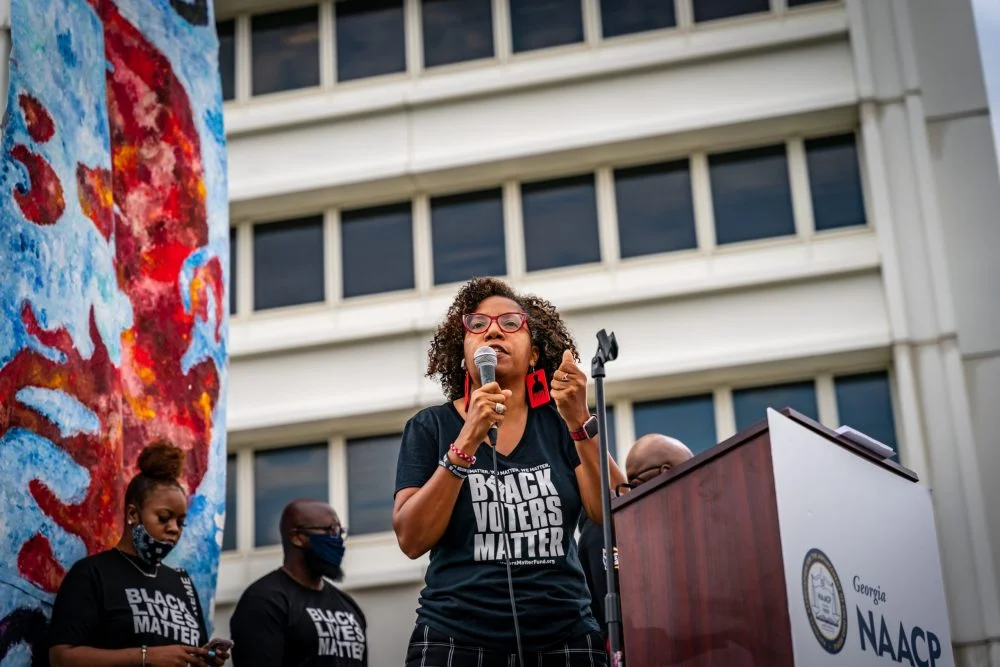 Photo of an activist giving a speech with a t-shirt of "Black Voters Matter"